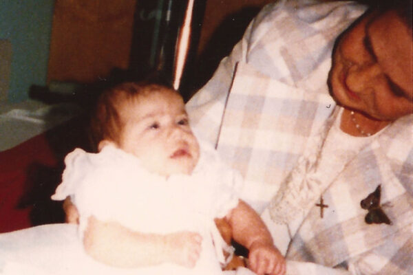 an older woman holding a baby in a baptism dress in 1985